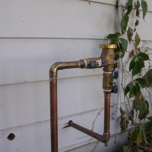 Copper piping with a brass valve and a plant in the background.