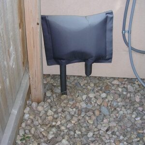 Small black protective cover over a pipe in a gravel area.